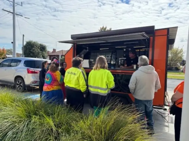 Customers gathered at the window of the Upside Down Coffee on the Go orange van being served hot coffee and cold drinks